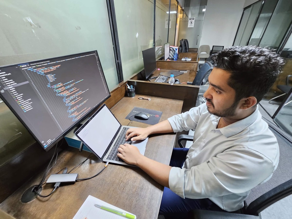 Ashekur Rahman working at a desk at Sumashtech, code open on an external monitor beside a laptop